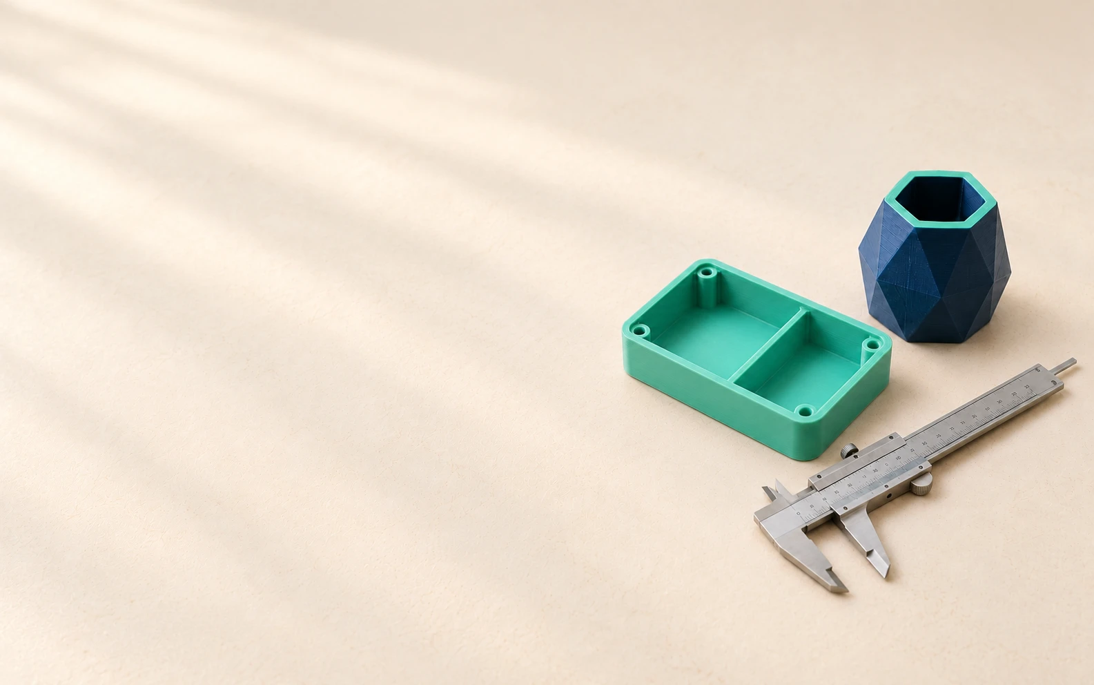 Piezas impresas en 3D en azul marino y menta, junto a una herramienta de medición para revisar sus dimensiones.
