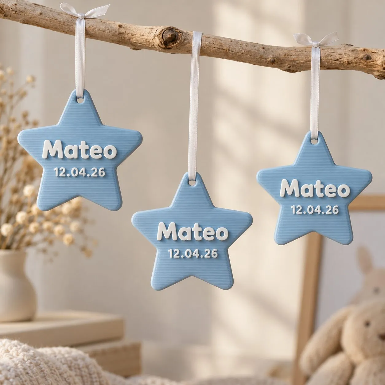 Tres estrellas celestes con el nombre Mateo y la fecha 12.04.26, colgadas con cintas blancas.