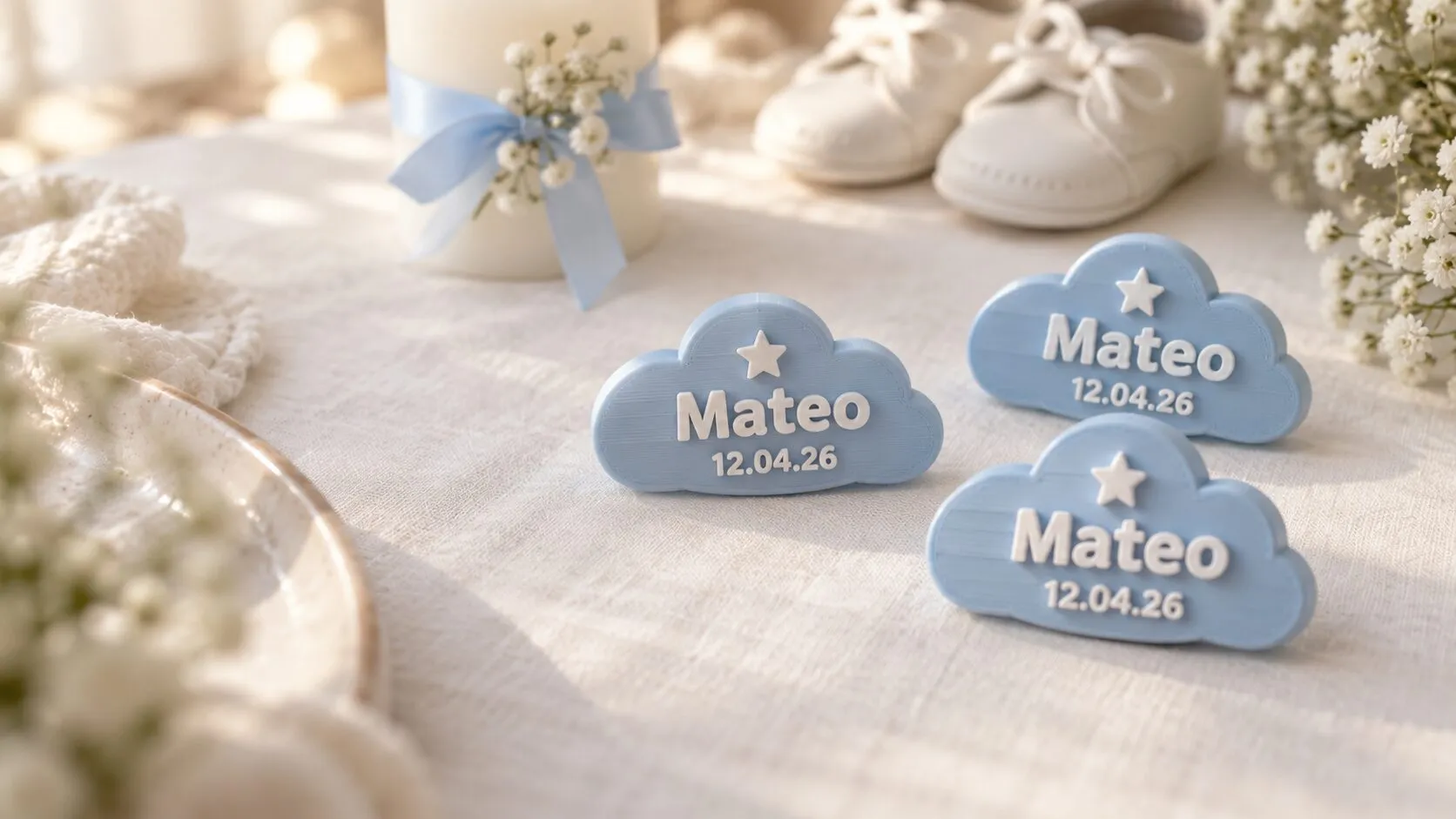 Tres recuerdos de bautizo celestes con forma de nube, con el nombre Mateo y la fecha 12.04.26, en una mesa con una vela y unos zapatitos blancos.