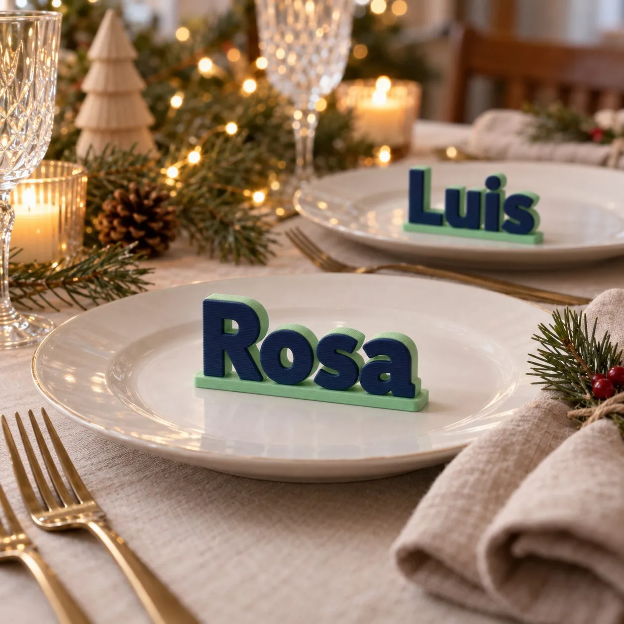 Dos platos en una mesa de Nochebuena, cada uno con un nombre en letras 3D azules: Rosa y Luis.